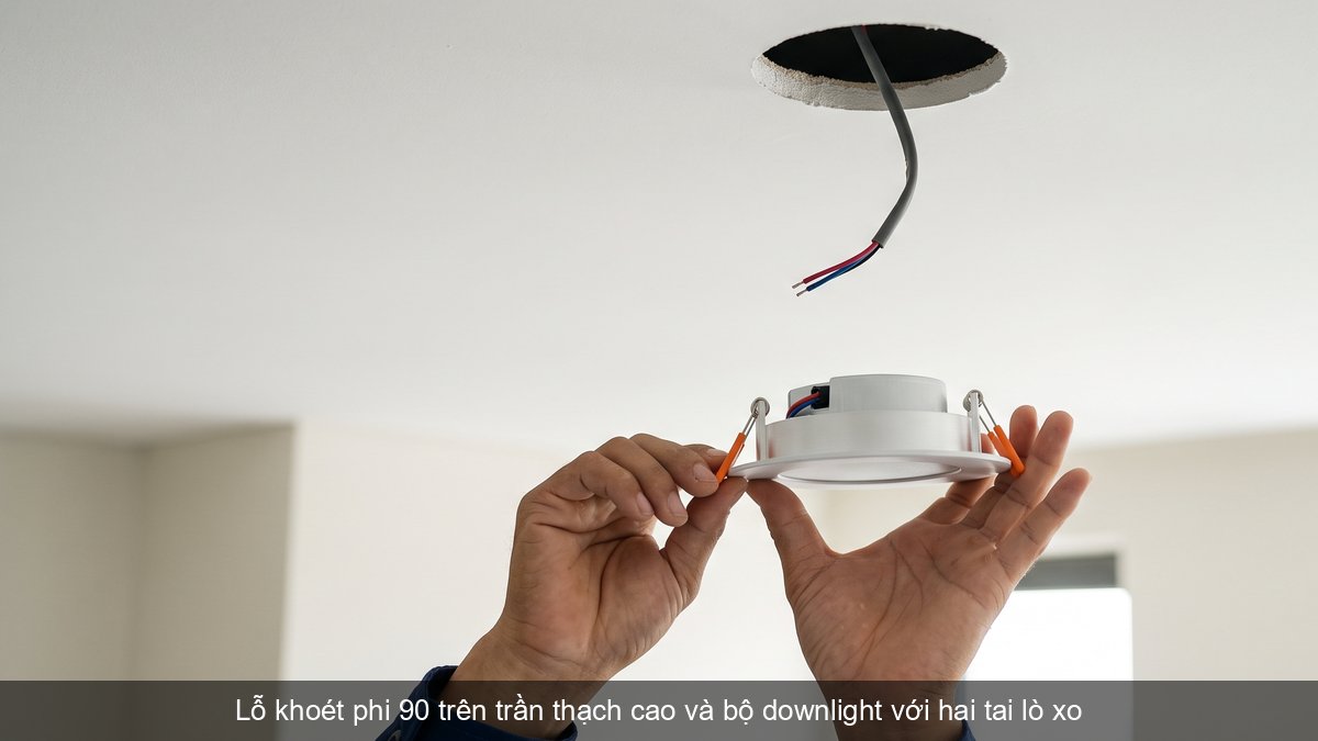 Thợ điện cầm bộ đèn downlight âm trần phi 90 có hai tai lò xo dưới lỗ khoét trần thạch cao